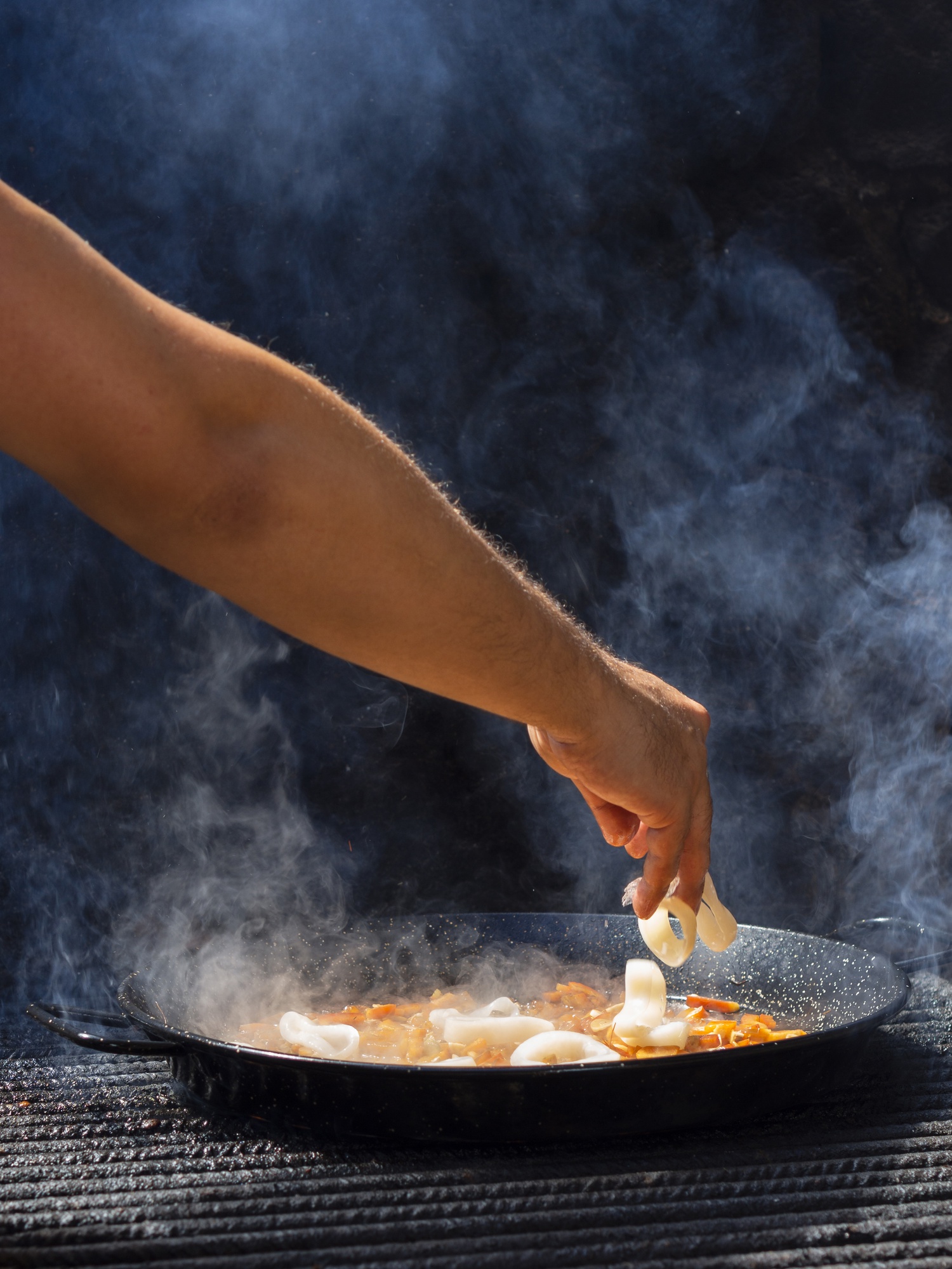 Cook adding calamari rings to vegetables on frying pan Free Photo
